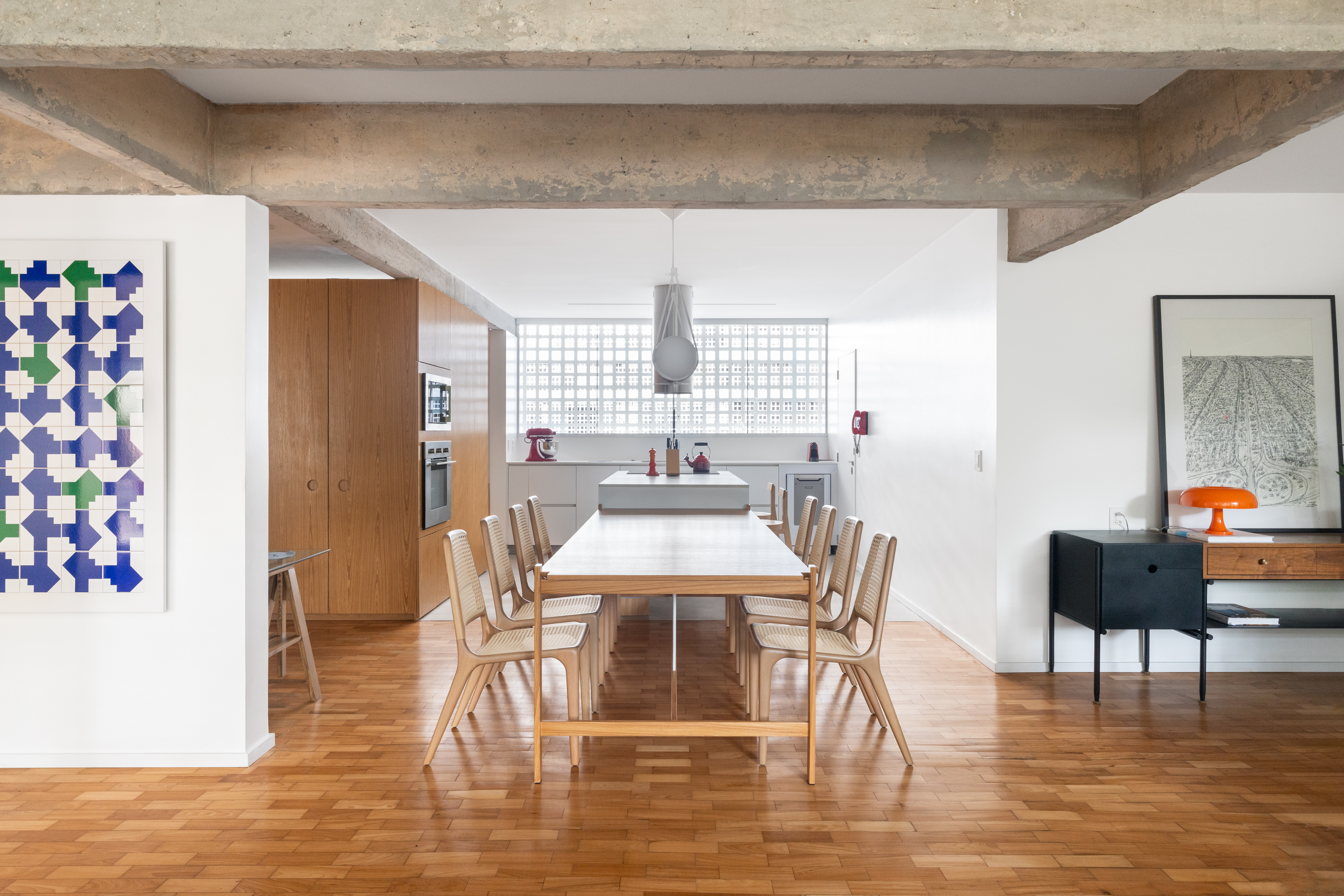 Reforma em apê de 150 m² valoriza a arquitetura modernista de Brasília. Projeto de Bloco Arquitetos. Na foto, sala de jantar com cadeira de palhinha, piso de madeira e cozinha.